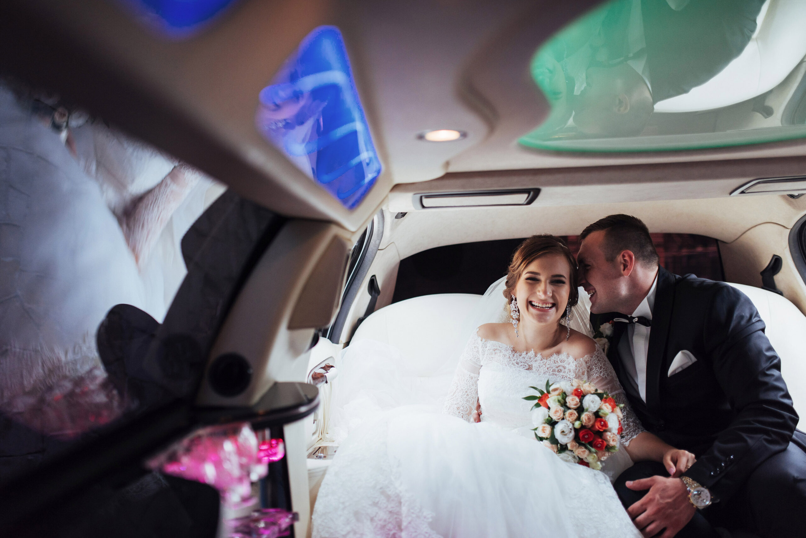 Un couple de mariés souriants à l’intérieur d’une limousine luxueuse le jour de leur mariage.